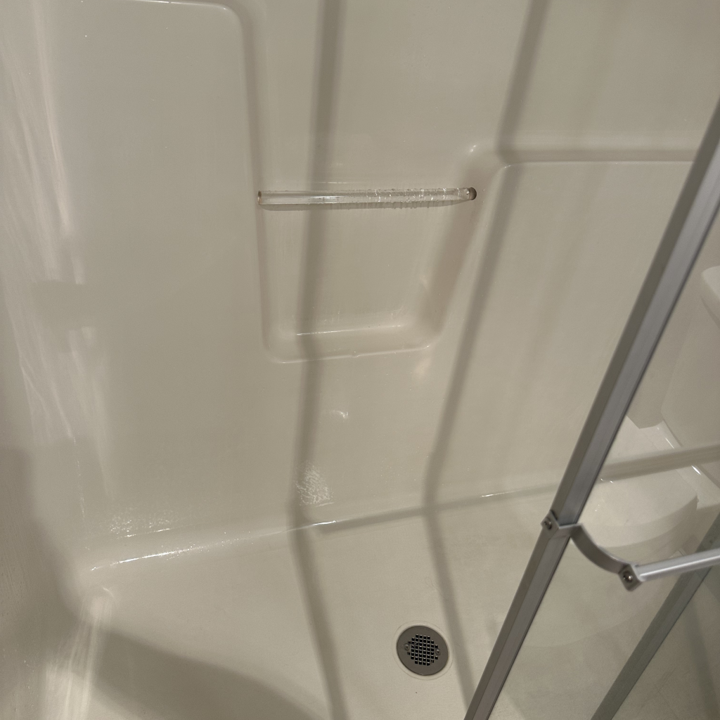 Interior of a clean, white shower stall with a glass door, featuring a built-in shelf and a drain at the bottom Interior of a clean, white shower stall with a glass door, featuring a built-in shelf and a drain at the bottom